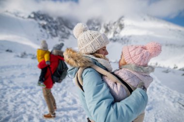 Aile dağlarda kış tatilinin tadını çıkarıyor. Karlı bir arazinin ortasında duruyor..