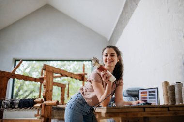 Tezgahta çalışan genç bir iş kadını, eski kumaşı dokumaya hazırlıyor. Döngülü tekstil, küçük kumaş dokuma işi ve dairesel ekonomi.