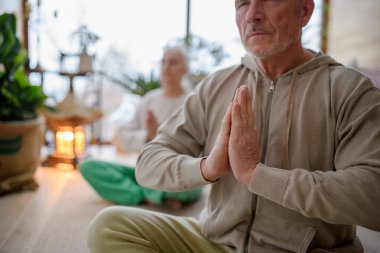 Yaşlı çift oturma odasında birlikte yoga yapıyor. Ev meditasyonları.