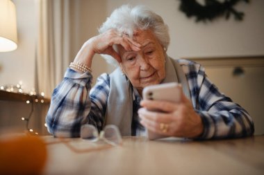 Akıllı telefon kullanmakta zorlanan yaşlı bir kadın, kafası karışmış görünüyor..
