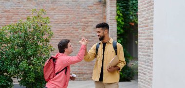 Down sendromlu genç bir adam ve akıl hocası arkadaşı selamlaşıyorlar, dışarıda duruyorlar.,