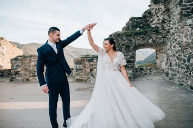 Gelin ve damat dans ediyor, birbirlerine bakıyorlar. Dışarıda yıkıntıların yanında duran güzel bir çift..