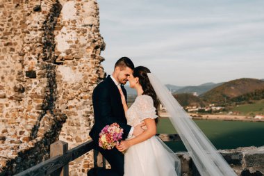 Gelin ve damat alınlarına dokunuyor, birbirlerine bakıyorlar. Dışarıda yıkıntıların yanında duran güzel bir çift..