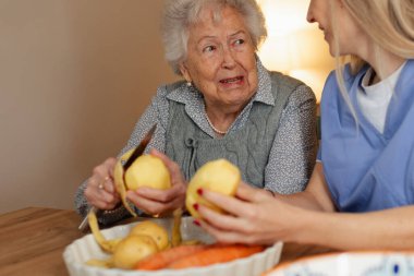 Yaşlı bir asistan ve patates soyan yaşlı bir kadının portresi. Evde sağlık hizmetleri.