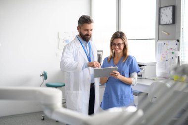 Doktor ve bayan hemşire tabletteki test sonuçlarına bakıyor. Doktorların ofisinde, klinikte sağlık çalışanları.