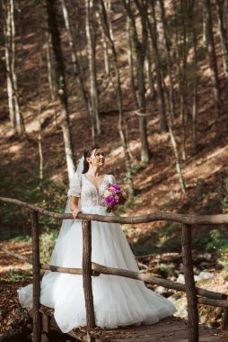Ormanla çevrili, kısa kollu, kar beyazı gelinliğiyle göz kamaştırıcı bir gelin..
