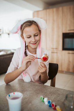 Girl with bunny ears paiting eggs for easter egg decorating. clipart