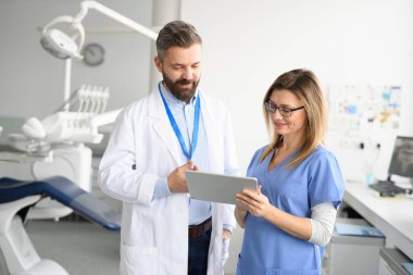 Diş hekimi ve bayan hemşire tabletteki randevu çizelgesine bakıyor. Doktorların ofisinde, klinikte sağlık çalışanları.