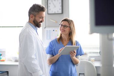 Doktor ve bayan hemşire tabletteki test sonuçlarına bakıyor. Doktorların ofisinde, klinikte sağlık çalışanları.