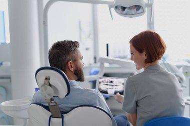 Dost canlısı bir dişçi, diş muayenesi sırasında hastaya röntgen gösteriyor..