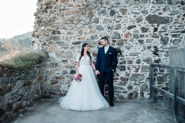 Gelin ve damat el ele tutuşup birbirlerine bakıyorlar. Dışarıda yıkıntıların yanında duran güzel bir çift..
