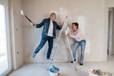 Üst düzey karı koca bir merdivenin üzerinde durmuş evlerinin duvarlarını boyuyorlar. Ev yenileme konsepti.