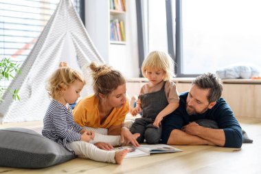Genç bir nükleer aile oturma odasında oyuncaklarla oynuyor. Ebeveynler ve çocuklar yerde yatar, çocuk hikayelerine, resimli kitaplara bakar, hafta sonunu evde geçirirler..