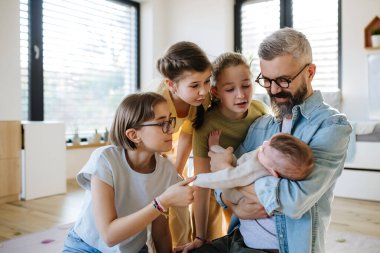 Üç kız kardeş babasının kollarında yeni doğan erkek kardeşe bakıyor. Büyük aile kavramı.