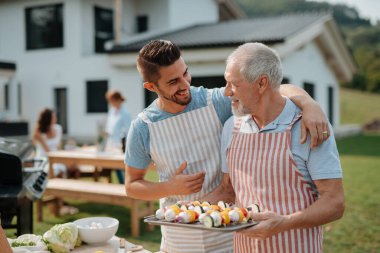 Kayınpederim ve damadım aile barbeküsü için yemek hazırlıyorlar. Bahar bahçesi partisi.