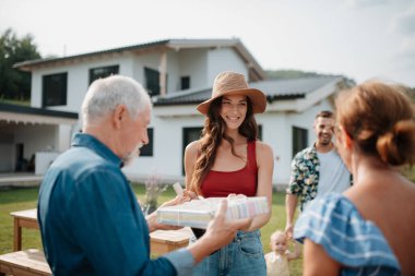 Gülümseyen genç bir kadın açık hava aile toplantısı sırasında hediye alıyor..