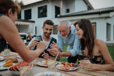 Yaşlı adam, Spring ailesinin barbekü partisinde akıllı telefondan fotoğraf gösteriyor. Aile bahçesi partisi.