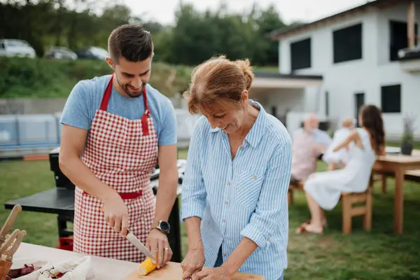 Yetişkin oğul ve büyük anne aile barbeküsü için yemek hazırlıyor..