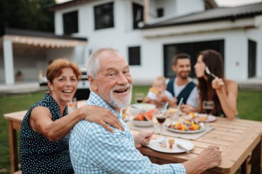 Aile masada oturuyor ve bahar aile barbeküsü sırasında lezzetli yemekler yiyor. Aile bahçesi partisi..