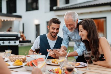Yaşlı adam, Spring ailesinin barbekü partisinde akıllı telefondan fotoğraf gösteriyor. Aile bahçesi partisi.