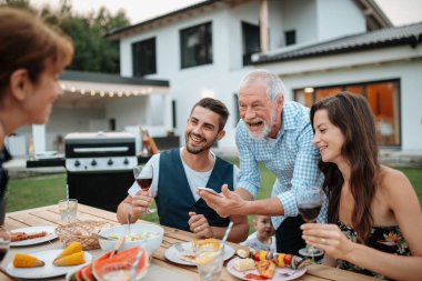 Yaşlı adam, Spring ailesinin barbekü partisinde akıllı telefondan fotoğraf gösteriyor. Aile bahçesi partisi.