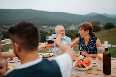 Aile masada oturuyor ve bahar aile barbeküsü sırasında lezzetli yemekler yiyor. Aile bahçesi partisi..