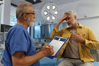 Muayene masasında oturan hasta, doktorlara sağlık sorunları ve semptomları anlatıyor..