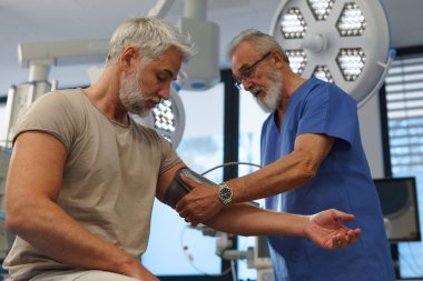 Doktor hastaların tansiyonunu dijital tansiyon monitörü kullanarak ölçüyor..