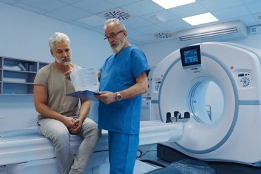 Doktor tomografi sonuçlarını hastane ortamındaki erkek hastaya açıklıyor.