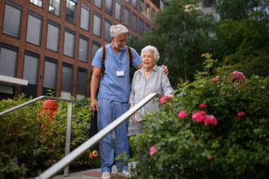 Sağlık görevlisi yaşlı bir kadının merdivenlerden inmesine yardım ediyor..