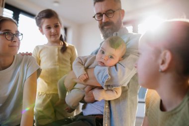 Üç kız kardeş babasının kollarında yeni doğan erkek kardeşe bakıyor. Büyük aile kavramı.