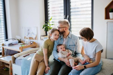 Üç kız kardeş babasının kollarında yeni doğan erkek kardeşe bakıyor. Büyük aile kavramı.