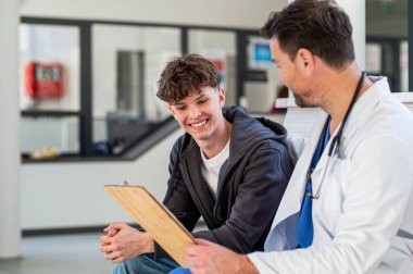 Genç çocuk gülümsüyor yardımcı doktorla konuşuyor, olumlu sağlık haberleri alıyor..