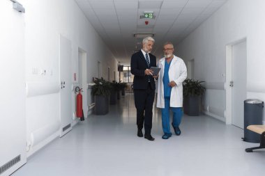 Doktor hastane müdürüyle konuşuyor, hastane koridorunda yürüyor..