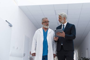 Doktor hastane müdürüyle konuşuyor, hastane koridorunda yürüyor..