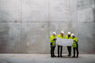 Mühendisler ve inşaat işçileri modern inşaat alanının planlarını inceliyor..