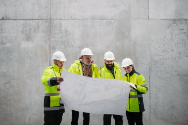 Mühendisler ve inşaat işçileri modern inşaat alanının planlarını inceliyor..