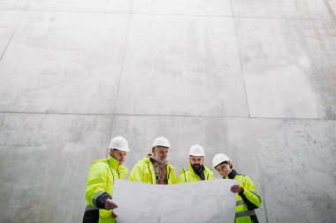 Mühendisler ve inşaat işçileri modern inşaat alanının planlarını inceliyor..