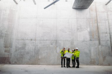 Mühendisler ve inşaat işçileri modern inşaat alanının planlarını inceliyor..