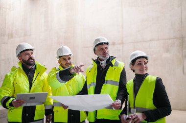 Mühendisler ve inşaat işçileri modern inşaat alanının planlarını inceliyor..