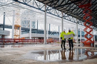 İnşaat yöneticileri mekanda dijital tablet kullanıyor, proje planlarını içeride gözden geçiriyorlar.