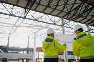 İnşaat yöneticilerinin bina planlarını veya proje planlarını gözden geçirmelerinin arka görünümü.