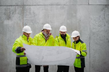 Mühendisler ve inşaat işçileri modern inşaat alanının planlarını inceliyor..