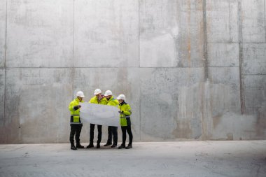 Mühendisler ve inşaat işçileri modern inşaat alanının planlarını inceliyor..