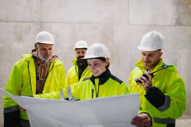 Mühendisler ve inşaat işçileri modern inşaat alanının planlarını inceliyor..