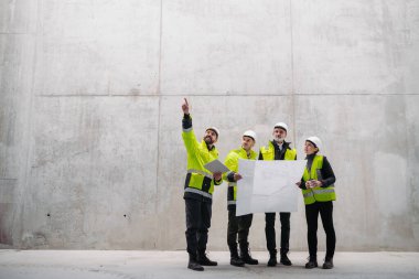 Mühendisler ve inşaat işçileri modern inşaat alanının planlarını inceliyor..