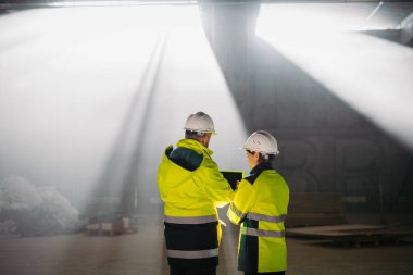 Mühendisler modern inşaat alanında bir tablet kullanarak inşaat planlarını tartışıyorlar.