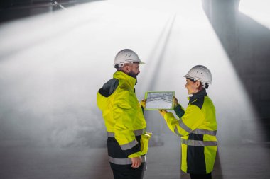 Mühendisler modern inşaat alanında bir tablet kullanarak inşaat planlarını tartışıyorlar.