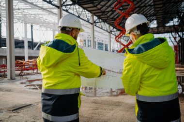 İnşaat yöneticilerinin bina planlarını veya proje planlarını gözden geçirmelerinin arka görünümü.