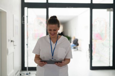 Hastanedeki dijital tablette hasta randevu listesini okuyan hemşire portresi.